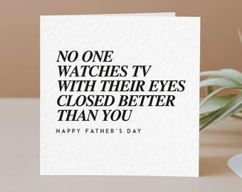 May include: A white Father's Day card with black text. The card reads "NO ONE WATCHES TV WITH THEIR EYES CLOSED BETTER THAN YOU" and "HAPPY FATHER'S DAY". The card is on a neutral background.