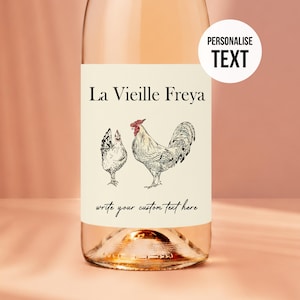 May include: A glass wine bottle with a cream-coloured label featuring a black ink illustration of a hen and a rooster with a red comb. The label displays the text La Vieille Freya and write your custom text here. A circular white badge reads PERSONALIZE TEXT.