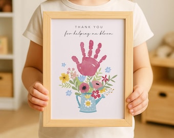 May include: A framed print with a light wood frame. The print features a pink handprint above a bouquet of flowers in a blue watering can. The text reads "THANK YOU for helping me bloom."