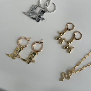 May include: A set of gold and silver jewelry featuring cowboy boot charms, balloon animal charms, and a snake charm. The jewelry includes earrings and a necklace.