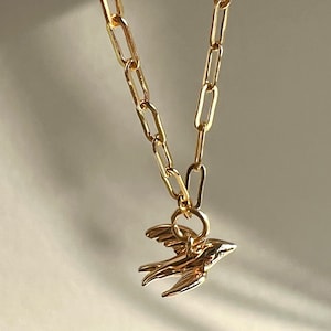 May include: A gold chain necklace with a small gold bird pendant.