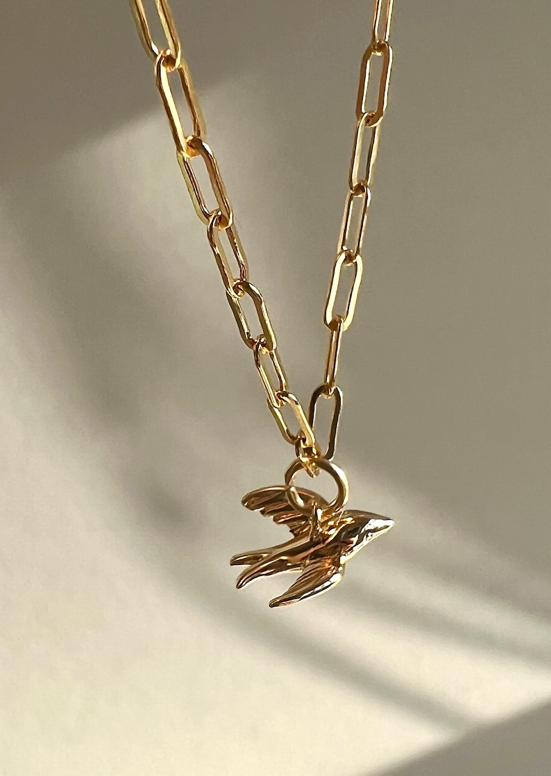 May include: A gold chain necklace with a small gold bird pendant.