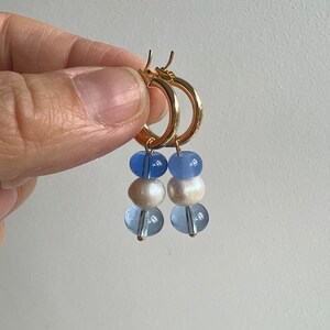 Pode incluir: Brincos de argola dourados com tr&ecirc;s contas azuis e brancas penduradas em cada argola.