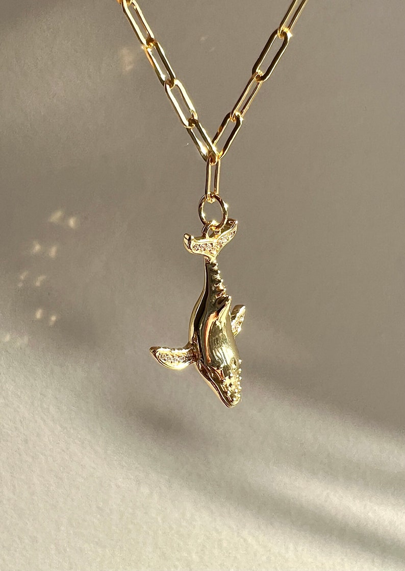 May include: A gold chain necklace with a whale pendant. The whale is detailed with small, clear stones.