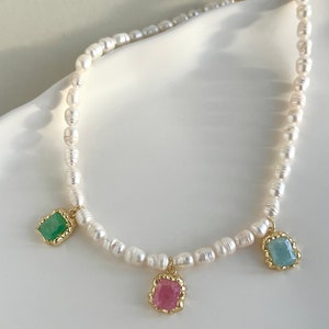 May include: A delicate pearl necklace with three dangling charms. The charms are square-shaped and feature green, pink, and blue gemstones.