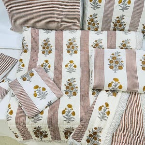 May include: A set of white and brown striped cotton bedding with a floral pattern. The bedding includes a quilt, pillowcases, and a throw pillow.