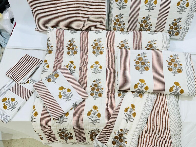 May include: A set of white and brown striped cotton bedding with a floral pattern. The bedding includes a quilt, pillowcases, and a throw pillow.