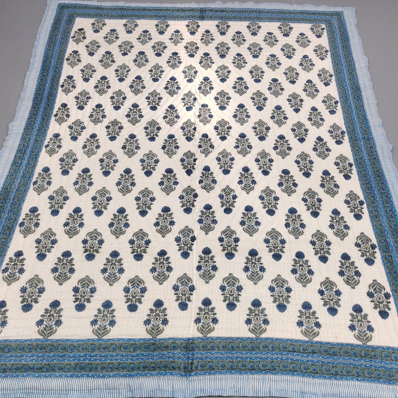 Op de afbeelding: Een wit katoenen dekbed met een blauw en groen bloemenpatroon. Het dekbed heeft een rand met een blauw en groen geometrisch patroon.