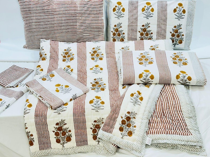 May include: A set of white and brown striped bedding with a floral pattern. The set includes a quilt, two pillowcases, and two smaller pillows.