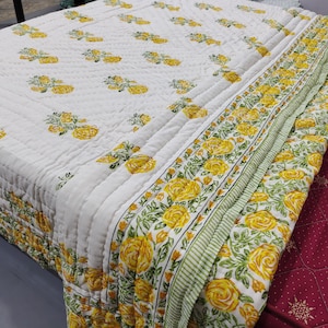 Può includere: Trapunta di cotone bianco con un motivo floreale giallo. La trapunta ha un bordo di strisce verdi e bianche con rose gialle.