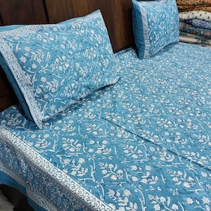 May include: A light blue bed sheet and two matching pillowcases featuring a white floral vine pattern. The bedding set includes a wide decorative border with a repeating scroll design along the edges of the fabric, creating a cohesive look.
