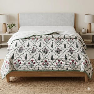 May include: A white and green floral quilt with a repeating pattern of flowers and trees. The quilt has a green border and is displayed on a wooden bed frame. The bed has a light gray headboard and white sheets.