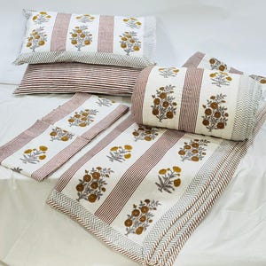 May include: A white and brown striped cotton quilt set with floral print. The set includes a quilt, two pillowcases, and a pillow sham.