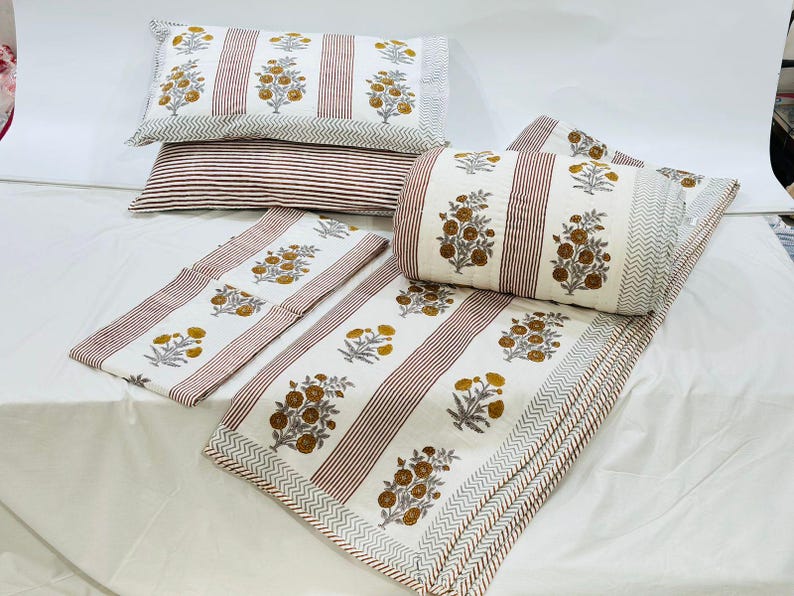 May include: A white and brown striped cotton quilt set with floral print. The set includes a quilt, two pillowcases, and a pillow sham.