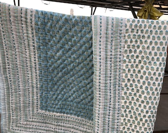 May include: A quilted cotton blanket featuring a reversible design with a light blue background and a white background, both decorated with repeating teal and green floral block print patterns and bordered by vertical striped geometric bands.