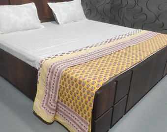 Könnte beinhalten: Ein Holzbettgestell mit einem weißen Bettbezug und einer gelben und roten gemusterten Bettdecke. Das Bett hat eine Schublade unter dem Bett.