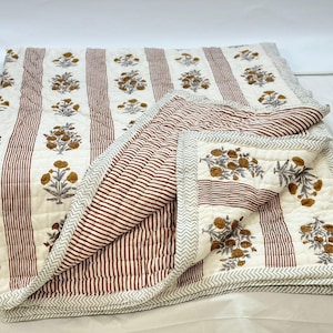 May include: A white and brown striped cotton quilt with a floral print. The quilt is folded in half and has a decorative border.