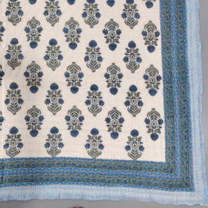 Op de afbeelding: Een wit katoenen dekbed met een blauw en groen bloemenpatroon. Het dekbed heeft een blauwe en groene rand met een witte streep.