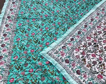 May include: A quilted bedspread featuring a vibrant turquoise background with a repeating floral pattern in shades of pink, dark purple, and green. The border displays a white background with a similar floral motif and a light blue chevron edge.