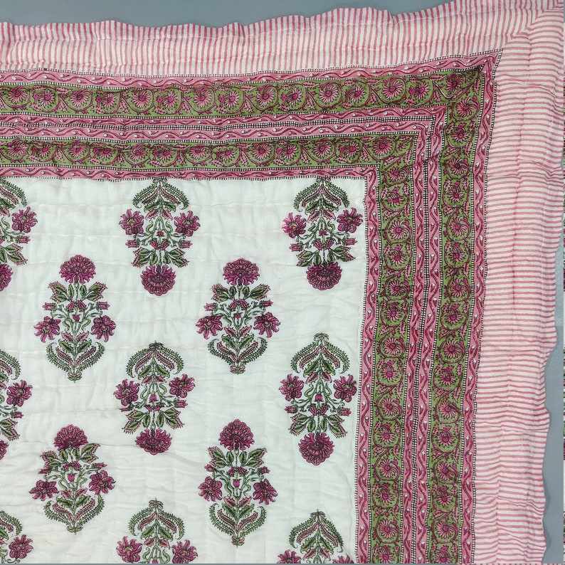 Op de afbeelding: Een wit katoenen dekbed met een roze en groene bloemenprint. Het dekbed heeft een rand met een herhalend patroon van roze en groen.