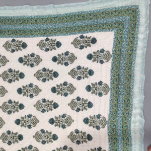 Op de afbeelding: Een wit katoenen dekbed met een groen en blauw bloemenpatroon. Het dekbed heeft een rand met een gestreept patroon.