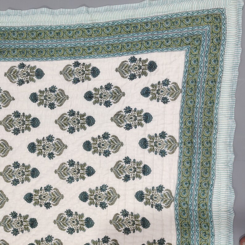 Op de afbeelding: Een wit katoenen dekbed met een groen en blauw bloemenpatroon. Het dekbed heeft een rand met een gestreept patroon.