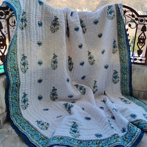 Può includere: Trapunta di cotone bianco con stampa floreale blu e bordo blu. La trapunta è piegata e drappeggiata su una ringhiera.