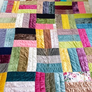 May include: A patchwork quilt made of various velvet fabrics in shades of pink, green, blue, brown, and yellow. The quilt is made up of squares and rectangles of different sizes and colors, creating a unique and colorful design.