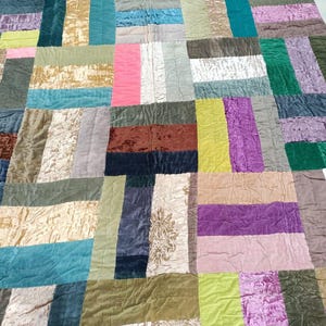 May include: A patchwork quilt made of various colors and textures of fabric. The quilt is made up of squares and rectangles of fabric, sewn together to create a unique design. The quilt is a mix of colors, including brown, green, blue, purple, and pink.