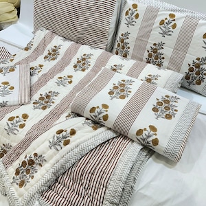 May include: A white and brown striped cotton quilt with a floral pattern. The quilt is made of multiple pieces, including a large quilt, two pillowcases, and two smaller pillows.