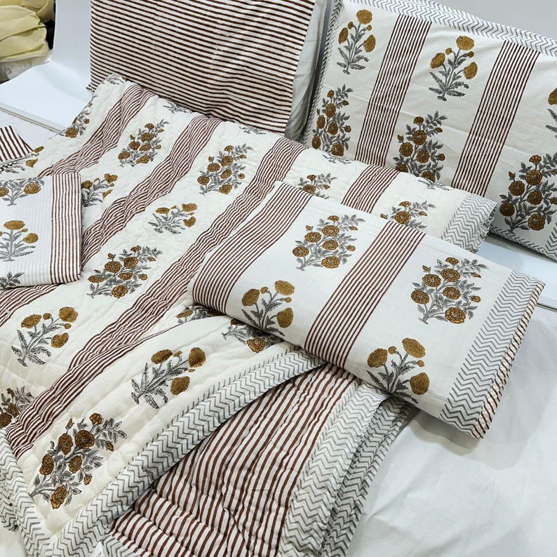 May include: A white and brown striped cotton quilt with a floral pattern. The quilt is made of multiple pieces, including a large quilt, two pillowcases, and two smaller pillows.