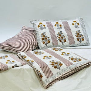 May include: A white and red striped bedding set with a floral pattern in shades of yellow and blue. The set includes a duvet cover, two pillowcases, and a throw pillow.