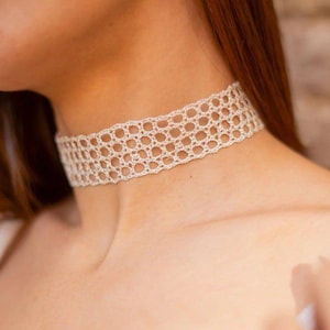 Peut inclure: Un collier ras de cou en crochet blanc avec un motif ajouré délicat.