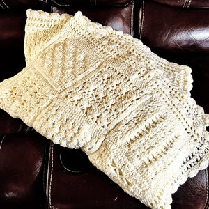 May include: A crocheted throw pillow with a cream-colored, intricate pattern. The pillow is made with a delicate, lacy stitch and has a slightly textured surface.
