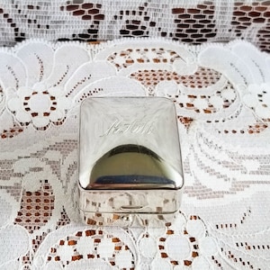 Peut inclure: Une boîte carrée en argent avec un couvercle à charnière. La boîte est gravée du texte "M.H. 1916".