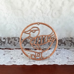 May include: A copper-coloured metal bird-shaped trivet with a circular design. The trivet is on a white lace tablecloth.