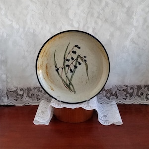 Peut inclure: Une assiette en céramique avec un glaçage moucheté brun et blanc. L'assiette présente un motif peint à la main de baies noires et de feuilles vertes.