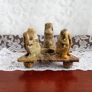 May include: Three carved stone monkeys, representing "See no evil, hear no evil, speak no evil", on a triangular base with a central candle holder.