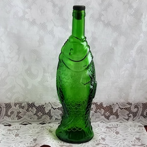 May include: A green glass bottle shaped like a fish. The bottle has a black plastic stopper.