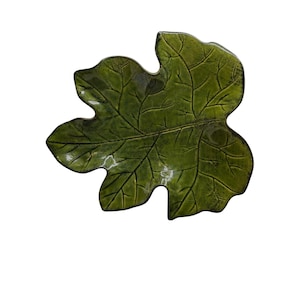 Puede incluir: Un plato de cerámica de color verde oliva brillante con forma de hoja grande de varios lóbulos. La superficie presenta un patrón de venas en relieve detallado que imita la estructura natural de una hoja de planta, con un acabado liso y reflectante.