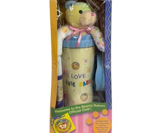 May include: A Beanie Babies travel mug kit in a cardboard box. The kit includes a plush bear with a yellow head and patterned arms, a light blue and cream travel mug with the text I LOVE BEANIE BABIES, sticker sheets, and markers.