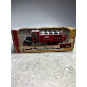 May include: A 1925 Kenworth stake truck die-cast metal model in a cardboard box. The truck is red with black fenders and wheels, featuring the True Value logo and text on the side. The box includes the text 1925 Kenworth Stake Truck w/Barrels.