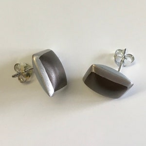 Könnte beinhalten: Ein Paar rechteckige Ohrstecker in Silber und Braun. Die Ohrringe haben ein schlichtes, modernes Design.