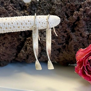 May include: A pair of silver earrings with a twisted design. The earrings are hanging from a white coral-like surface.