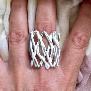 Könnte beinhalten: Ein silberner Ring mit einem geflochtenen Design. Der Ring ist breit und hat ein geometrisches Muster.