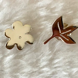 Könnte beinhalten: Ein Paar silberne Ohrringe, einer in Form einer Blume und der andere in Form eines Blattes.