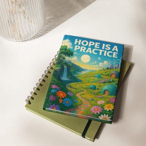 May include: A spiral-bound notebook with the text "HOPE IS A PRACTICE" on the cover, featuring a colorful landscape illustration. The image includes a waterfall, flowers, and small dome-shaped houses. A second green notebook is beneath it.