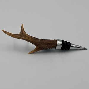 May include: A brown antler bottle stopper with a silver and black metal top. The antler is polished and has a natural finish.
