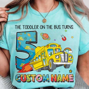 May include: A light blue t-shirt with the text "THE TODDLER ON THE BUS TURNS 5 CUSTOM NAME". The number 5 is filled with a space-themed design. A yellow school bus with a rocket flame is featured.