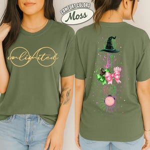 May include: Olive green t-shirt with the word "unlimited" in gold script inside two gold circles. The back of the shirt features a witch hat, bow, and other graphics in green, pink, and black. The shirt is labeled "Comfort Colors Moss".